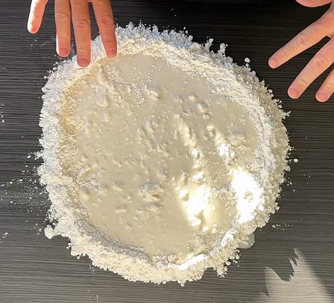 Handen bij een berg bloem met een kuiltje water: het begin van het pizzadeeg
