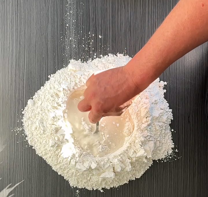 Een hand mengt water door een kuiltje bloem: zo begint het pizzadeeg