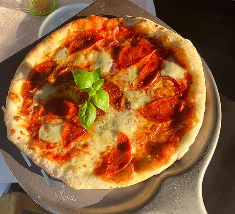 Pizza met salami, mozzarella en een toef basilicum op een pizzaschep